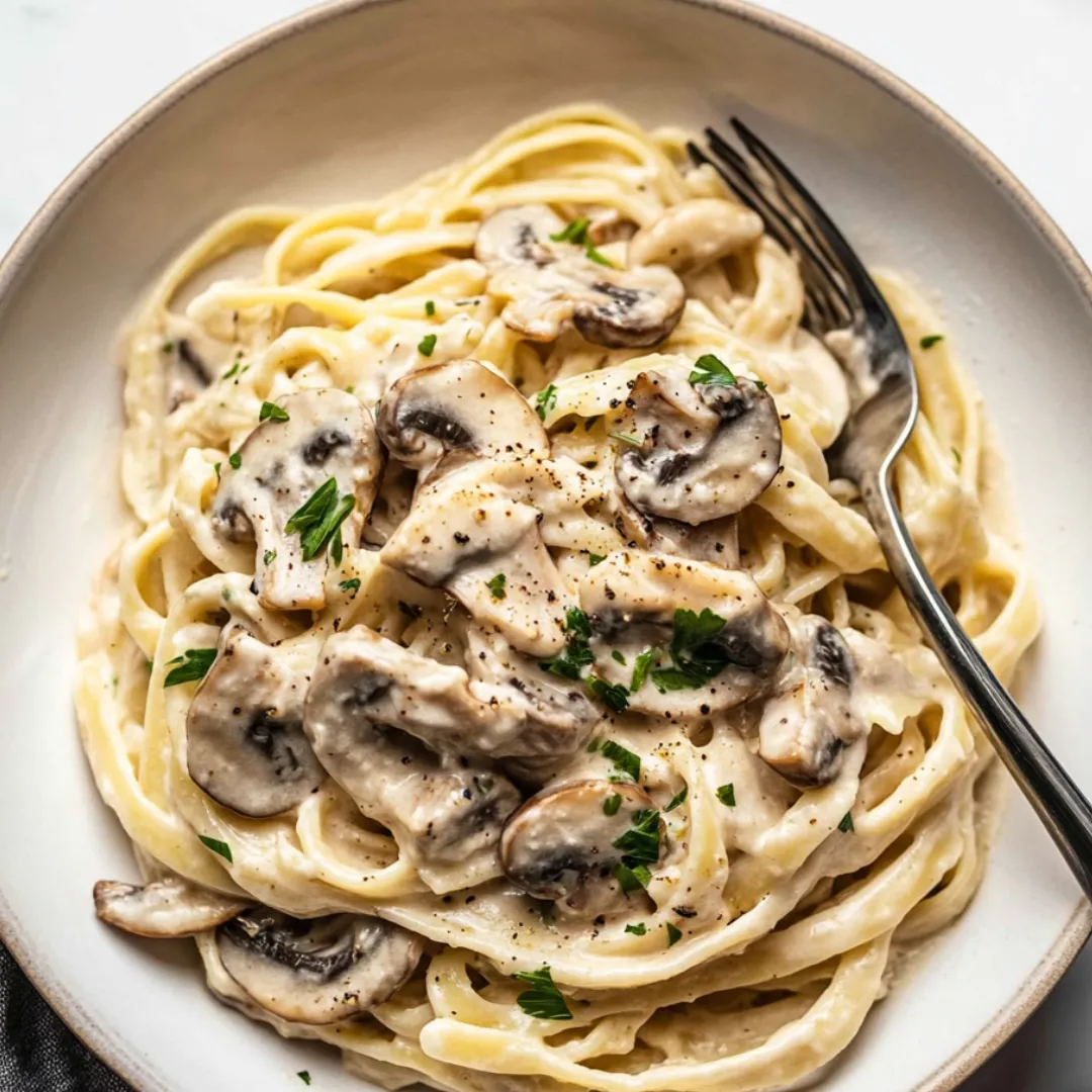 Pasta piled on a plate with mushrooms and fresh herbs on top.