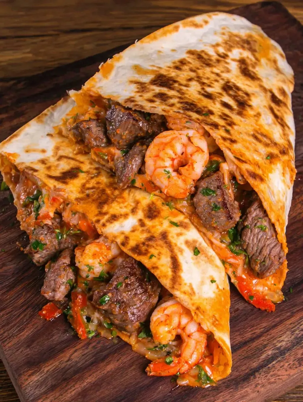 A burrito packed with shrimp and steak on a wooden table.