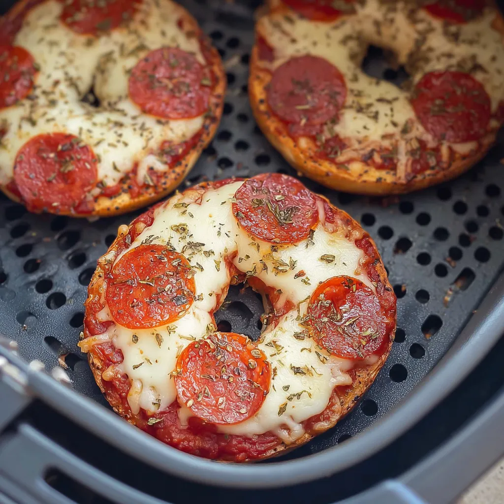 Two pepperoni bagels cooking on a rack.
