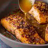 A skillet filled with salmon while honey is being spooned on top.