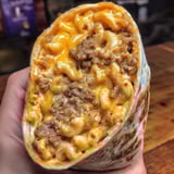 A hand clutching a burrito bursting with creamy mac and cheese.