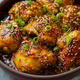 A bowl with orange-glazed chicken and sliced green onions.