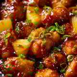 A close-up shot of chicken topped with pineapple and a sprinkle of bright herbs.